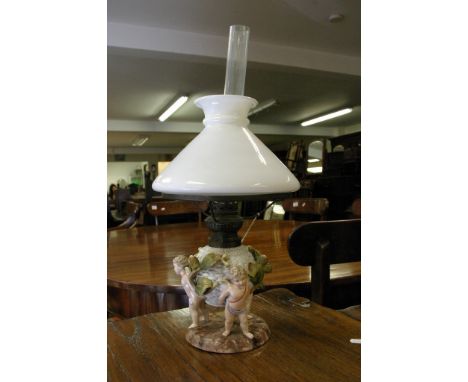 A late 19th Century Sitzendorf oil lamp supported with three putti with raised foliage with milk shade and clear funnel. 