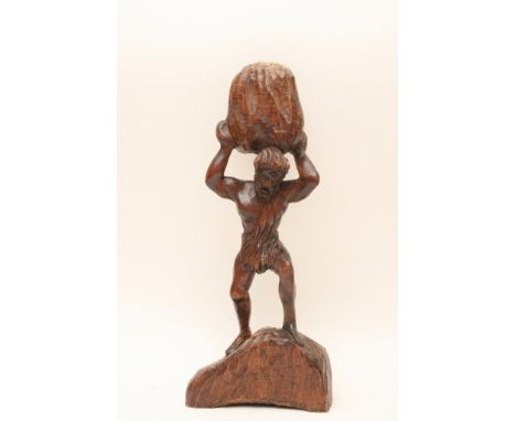 An antique mythological carved figure of a muscular bearded man holding a large rock or boulder above his head, possibly a de