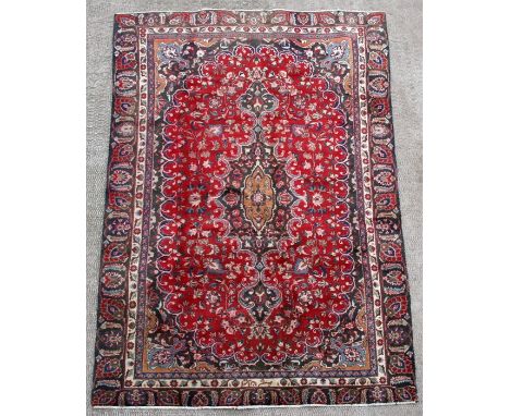 A Persian Mashad woollen hand knotted carpet with central floral medallion within floral borders on a red ground, 266 by 160c
