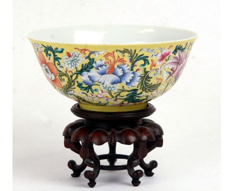 A Chinese famille rose bowl decorated with flowers on a yellow ground, blue seal mark to the underside, on a hardwood five-le