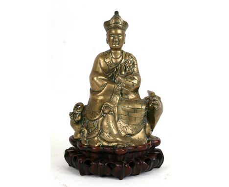 A Chinese bronze figure depicting a robed figure seated on a mythical beast, mounted on a hardwood stand, 33cms (13ins) high.