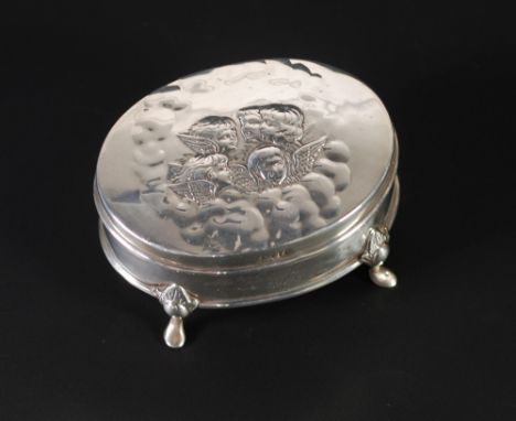 EDWARDIAN SILVER TRINKET OVAL BOX, with lid embossed with angelic faces, raised on four scroll supports, with blue plush lini