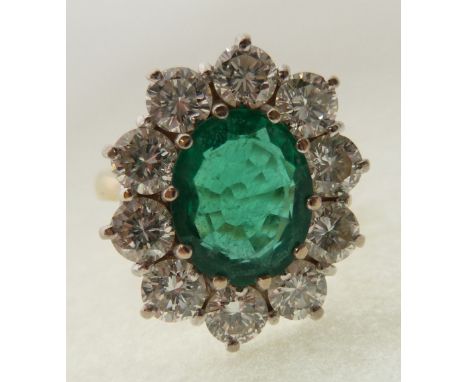 EMERALD AND DIAMOND CLUSTER RING, claw set with an oval cut emerald (possibly synthetic) with a cluster surround of ten round