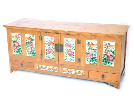 A Chinese pine low cabinet, with a plank top above two doors flanked by four panels, each inset with handpainted tiles decora