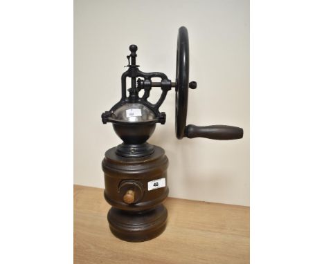 A 20th century manually operated coffee grinder, the cast metal mechanism with large wheel over the tuned wood base