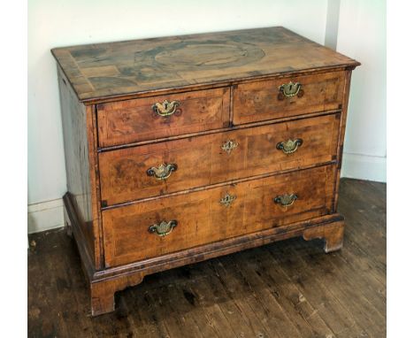 A George I walnut chest of drawers, early 18th century, the quarter veneered top with central oval panel, over two short and 