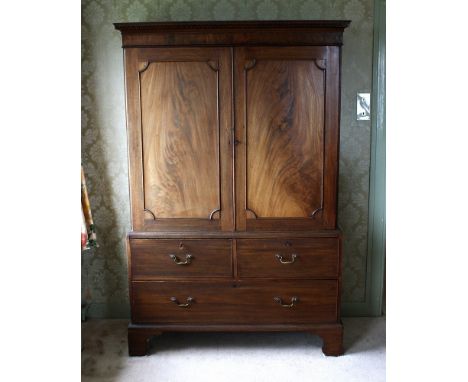  A late-Georgian mahogany linen press, the top with flared and moulded dentil cornice over two flame mahogany figured doors, 