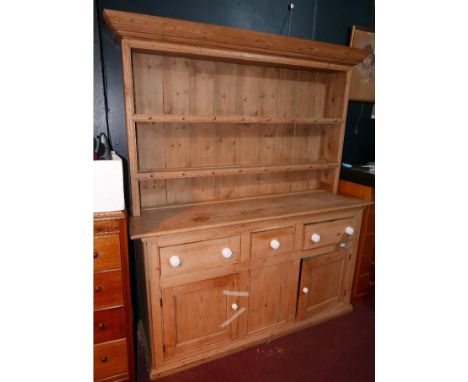 An early 20th century pine Welsh dresser, with three drawers over three cupboard doors, having white ceramic handles, raised 