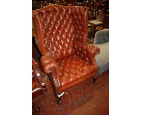 A Georgian style red leather wing armchair with button back and carved legs  