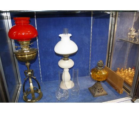 A Victorian white opaline oil lamp, a Victorian brass lamp with bright red glass shade and a cast iron based oil lamp with ye