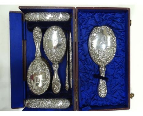 A cased seven-piece silver-mounted dressing table set embossed with flowers with etched letter 'D', Birmingham 1899/1900/1903