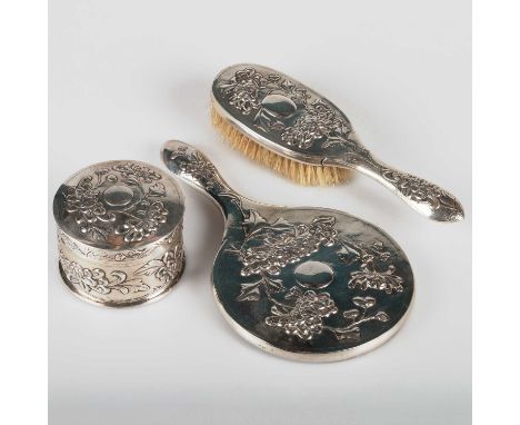 A CHINESE SILVER DRESSING TABLE SET mark of Yong Sheng, comprising covered box, brush and mirror, each embossed with flowers.