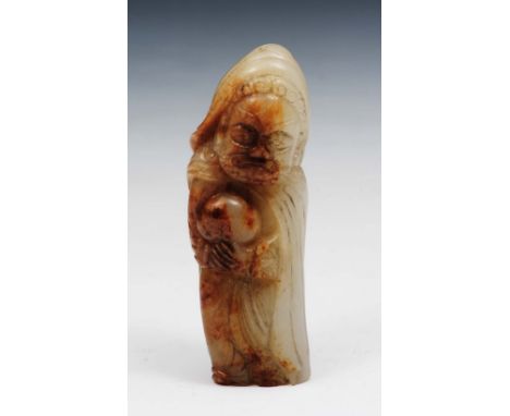 A Chinese white and russet jade of an Immortal 17th Century the Immortal standing holding a stone with both hands, wearing fl