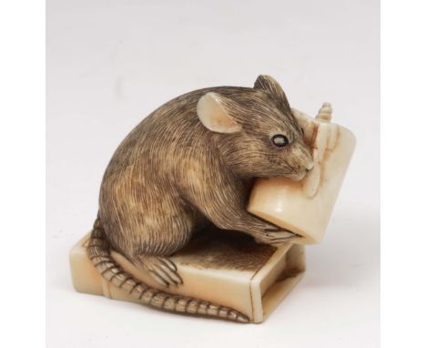 A Japanese ivory netsuke of a rat 19th Century signed Hoichi, the rat holding a partially used candle seated upon an open mat