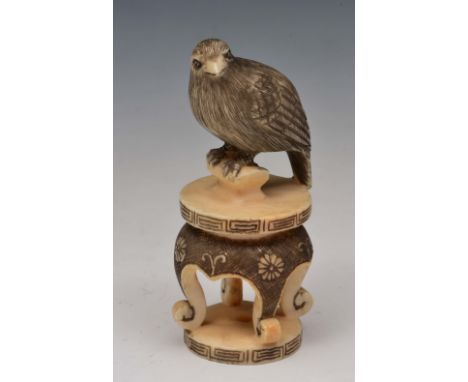 A Japanese ivory netsuke of a bird of prey Meiji period signed Harunobu, modelled on a four legged stool decorated with flowe