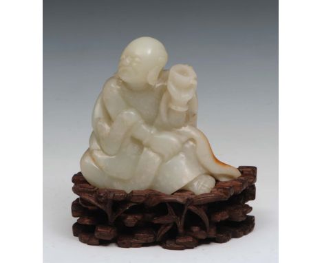 A Chinese white and rust brown jade pebble 18th Century carved as a seated Lohan looking to the right and holding a begging b