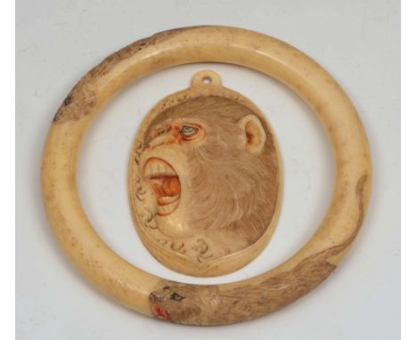 A Japanese ivory bangle Meiji engraved with lions and a Japanese ivory oval pendant carved with the head of a monkey (2)