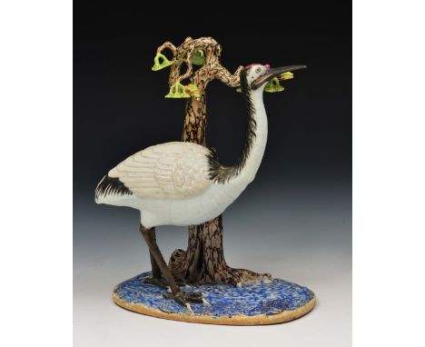 A Chinese porcelain model of a crane 19th Century standing against a trunk, on an oval base, 23cm high