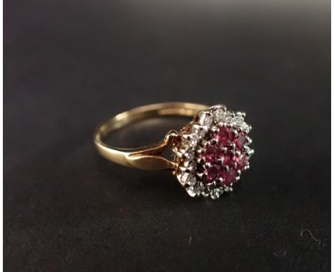 A Ruby Cluster Ring peg-set a group of seven round rubies within a frame of white stones in 9ct gold, ring size J 1/2 