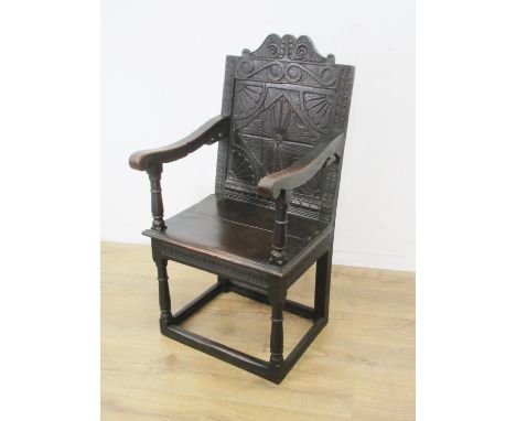 A 17th Century oak Armchair with scroll carved top rail and frieze above rosette panel back having fan spandrels, shaped arms