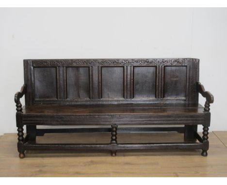 A 17th Century oak Settle with scrolled leafage carved cresting rail above five panel back mounted upon bobbin turned front s
