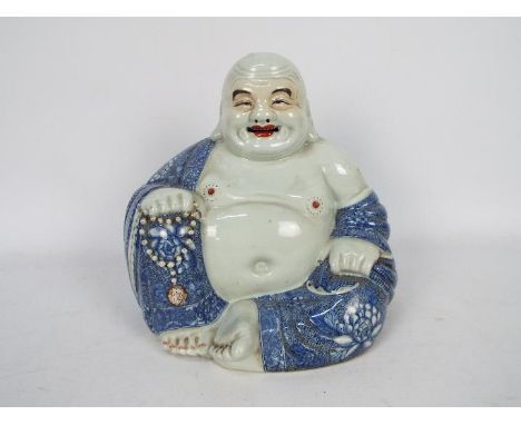 A Chinese figure of Budai, modelled in open robes, clutching prayer beads in one hand and carrying his sack in the other, imp