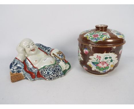 A Chinese ceramic model depicting Budai in reclining pose clutching a string of gilt beads, his robe decorated with auspiciou