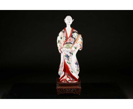 A Japanese Edo period porcelain figure of a Bijin with tied hair and wearing a floral and fan painted kimono in iron red, cob