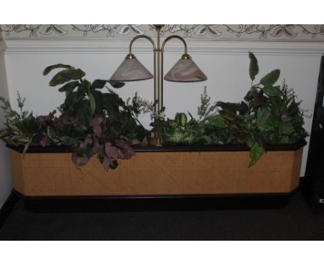 A canted oblong caned and stained wood planter, housing a variety of artificial plants and centred by a three branch light fi