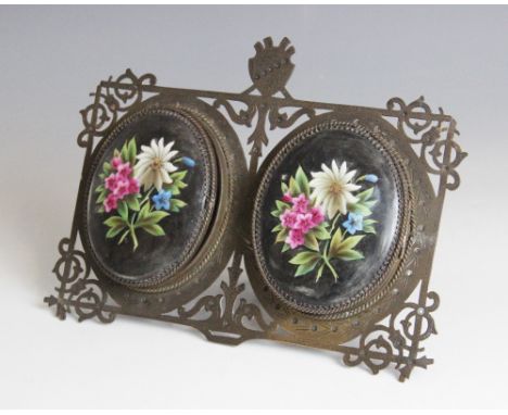 A Victorian brass double photograph frame, each aperture of oval form with hinged covers set with ceramic panels decorated in