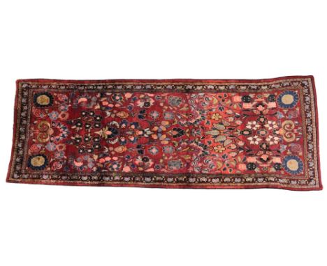An Iranian floral pattern wool runner, the central red field overlaid with multi coloured floral sprays within repeating bord