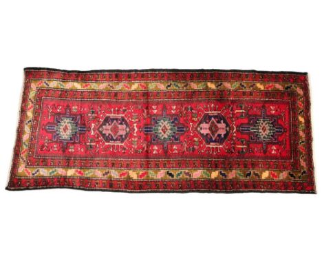 An Iranian Heriz type wool runner, the five central geometric medallions on a vibrant red field, enclosed by three repeating 