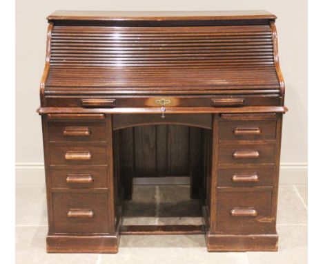 An early 20th century oak roll top desk, the tambour front opening to an arrangement of small drawers and pigeon holes, above