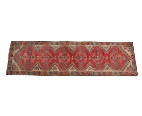 A Caucasian hand knotted wool runner, in red, ivory and blue colourways, the central field with six repeating geometric medal