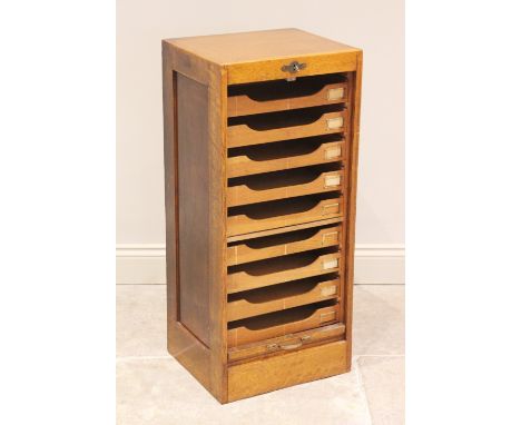 An early 20th century tambour front oak filing cabinet, the tambour drop front opening to nine sliding trays, each applied wi