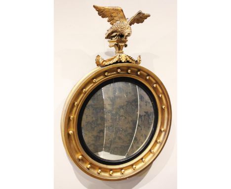 A Regency style giltwood circular wall mirror, 19th century, the eagle crest above the convex mirrored plate, within an eboni