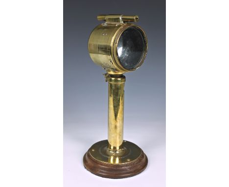 A WWII or earlier brass signalling lamp, mounted on circular wooden mount, having broad arrow mark, the plaque to the side re