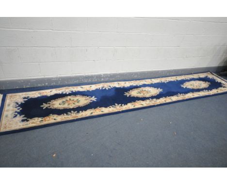 A WOOLLEN CHINESE CARPET RUNNER, with a dark blue field, 417cm x 77cm (condition:-some stains, see images)