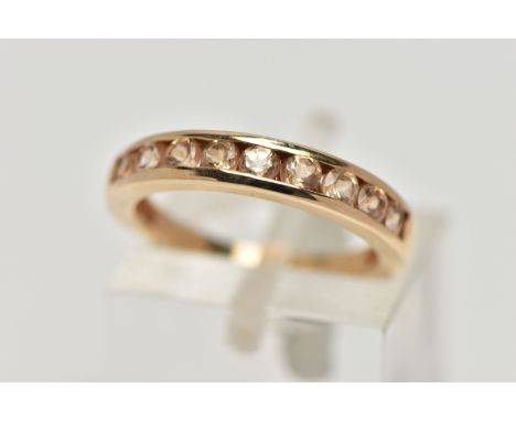 A 9CT GOLD GEM SET HALF ETERNITY RING, the circular shape peachy colour gems assessed as tourmaline, within a channel setting