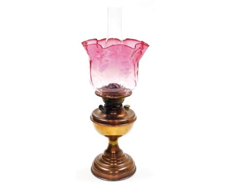 An early 20thC oil lamp, with a graduated pink clear glass shade and a brass central reservoir, on a brass tapering foot, 51c