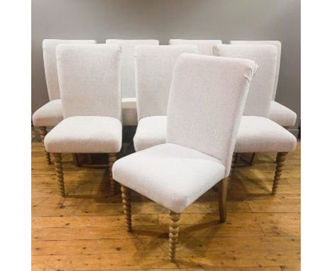 A set of eight light oak dining chairs with padded backs and seats, covered in a pale fleck linen style material on graduated