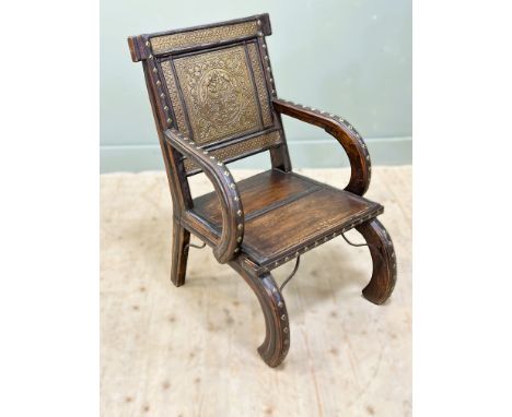 A Indian hardwood brass embossed panel mounted and studded open armchair on curved scroll supports (h. 86cm x l. 58cm x d. 55