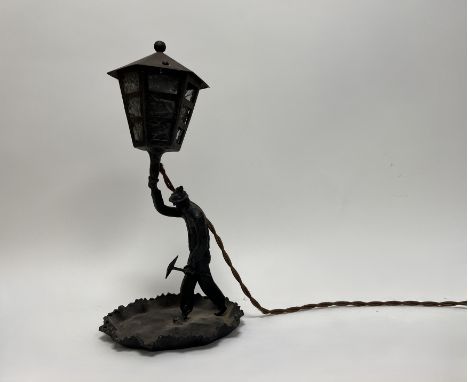 A spelter table lamp in the form of a miner with large street lantern light shade and clouded glass panes (one pane a/f) (h. 