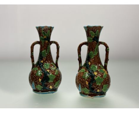 A pair of majollica style twin handled bud vases, in the style of a trunk with crawling vine leaves, chips to rim and base. (