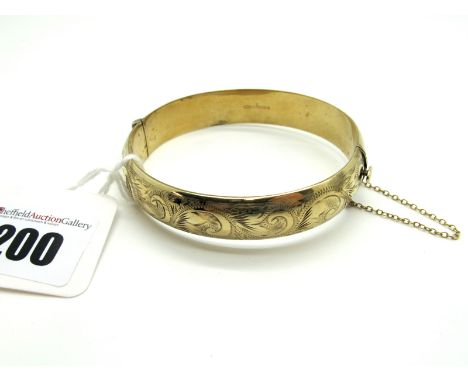 A 9ct Gold Bangle, leaf scroll engraved to the front, hinged to snap clasp.