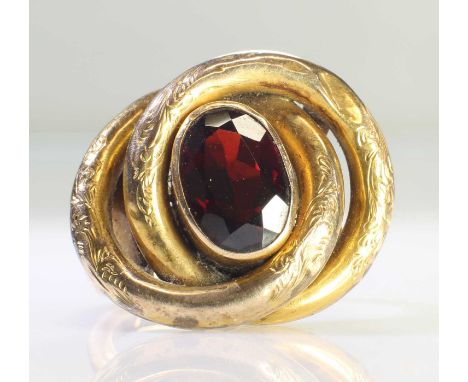 A GARNET RING converted from a brooch, the oval garnet within a foliate engraved lover's knot frame, to a later shank. Marked