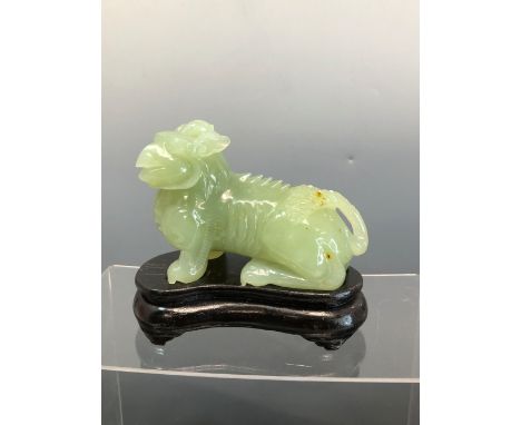 AN ORIENTAL CARVED JADE GREEN HARDSTONE FIGURE OF A GRIFFIN ON A WOODEN BASE. 