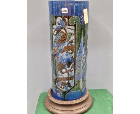 A BRANNAM STYLE POTTERY CYLINDRICAL STICK STAND ON A WOODEN PLINTH, THE SIDES DECORATED WITH TWO EXOTIC BIRDS IN BLUE GREEN A