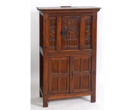 An early 17th century style oak cupboard, carved a crest and linen fold panels, having a door above a pair of panel doors, on