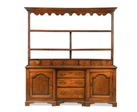 An oak dresser, 18th century, the moulded cornice above a shaped frieze with two open shelves over seven small drawers, the l